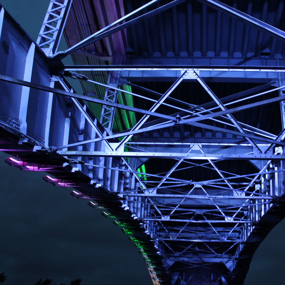 Photo of the structure underneath a bridge, shown lit up at night time